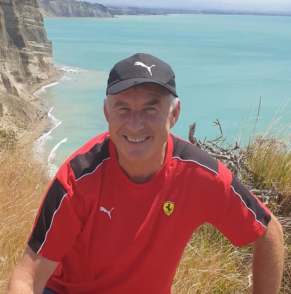 a man in a red shirt and black hat sitting on a cliff overlooking a body of water