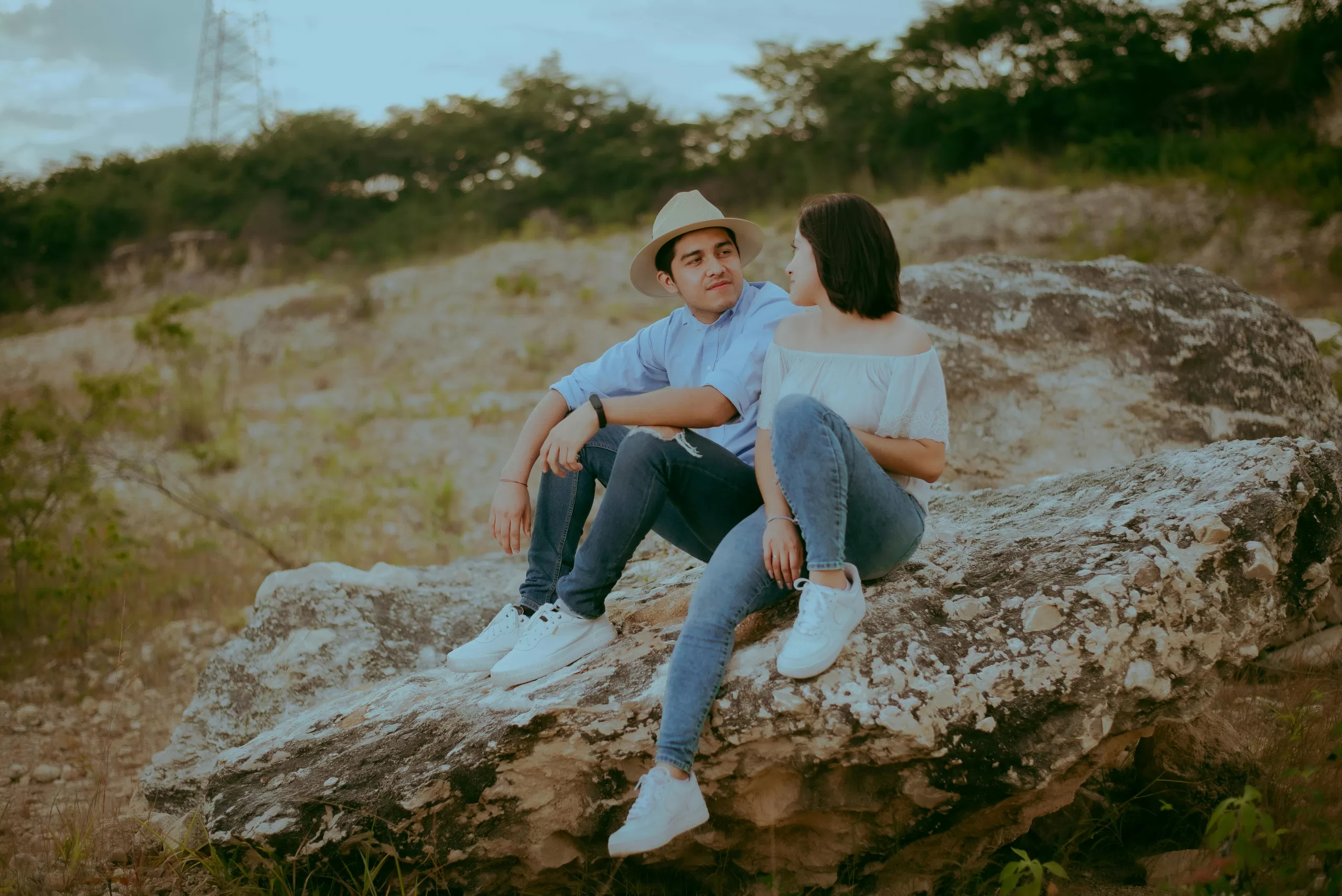 A couple sitting together on a rock, sharing a romantic moment outdoors.